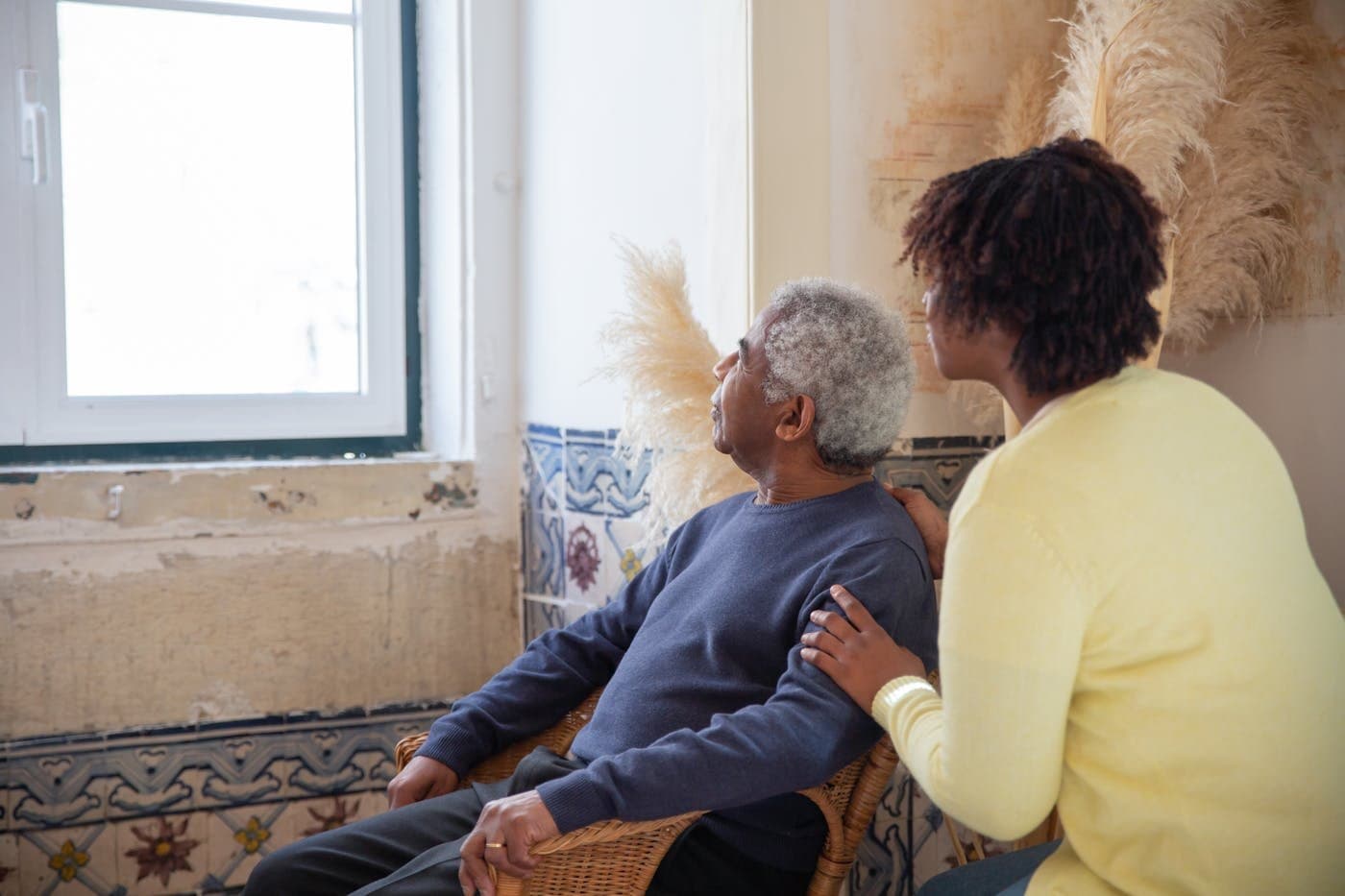Adult daughter sitting supportively with an elderly parent by the window