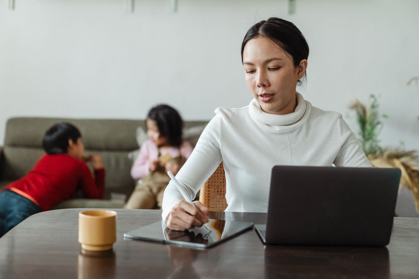 Mother working on a laptop while her children play in the background