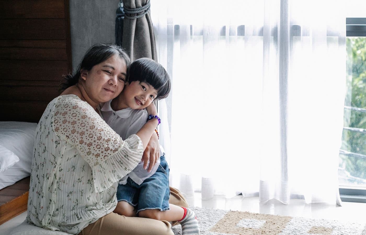Grandmother hugging her young grandson in a sunlit bedroom