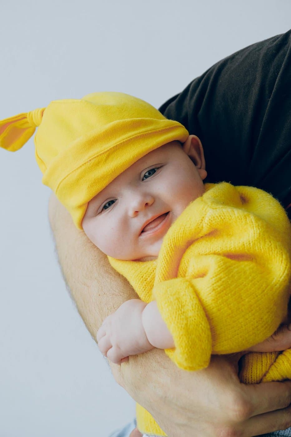 Smiling baby in a yellow knit outfit held close by a parent