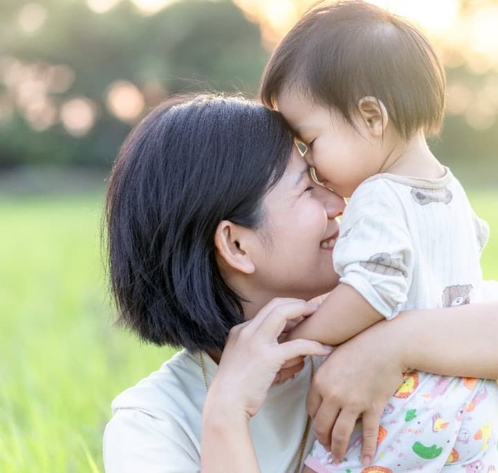 East Asian mother and toddler sharing an affectionate nose-to-nose moment outdoors in golden sunlight