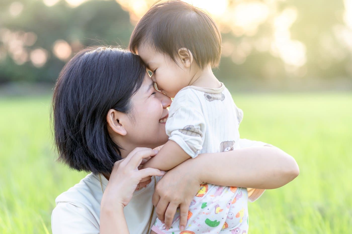 East Asian mother and toddler sharing an affectionate nose-to-nose moment outdoors in golden sunlight